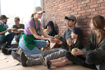 Volunteers giving food to poor people indoors - obrazy, fototapety, plakaty