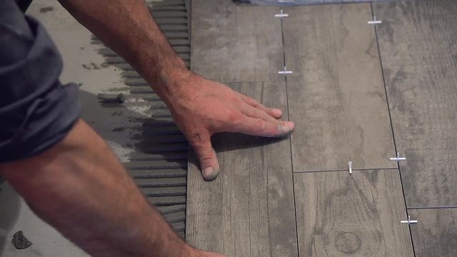 laying tile on the floor, ceramic tile laying, pressing down and regulating, installing plastic industrial crosses for fixing, Professional worker laying tiles on floor