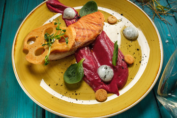 Baked salmon fillet with tomato sauce and cream sauce in bags decorated with greens and edible chips on an orange plate standing on a blue background