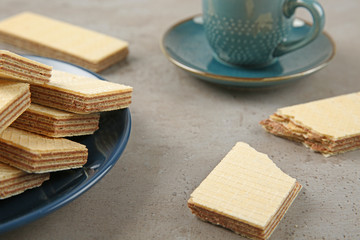 Plate of delicious wafers with cup of drink on grey stone background, closeup