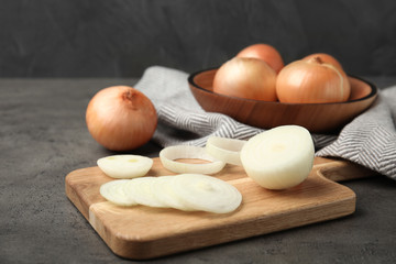 Wooden board with cut onion and bowl of bulbs on grey table
