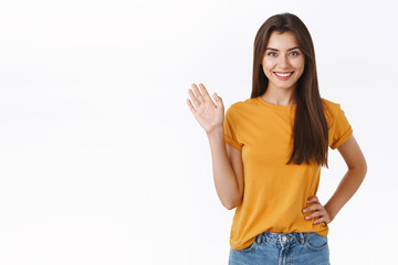 Friendly cheerful, happy smiling woman waving you with raised hand. Attractive girl greeting friend, say hello or hi, welcome guest, standing white background joyful, express positivity and joy © Cookie Studio