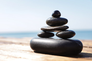 Fototapeta na wymiar Stack of stones on wooden pier near sea, space for text. Zen concept
