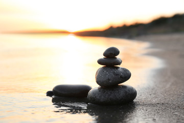 Dark stones on sand near sea at sunset, space for text. Zen concept