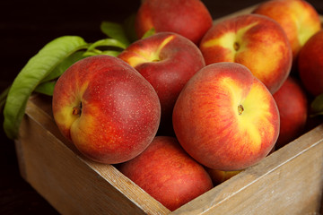 Wooden crate with tasty peaches and leaves on black background