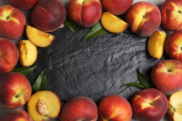 Frame made of fresh peaches and leaves on slate plate, flat lay with space for text