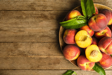 Plate with tasty fresh peaches and leaves on wooden table, top view. Space for text - obrazy, fototapety, plakaty