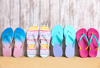 Different bright flip flops on sand near wooden wall, space for text. Summer beach accessories