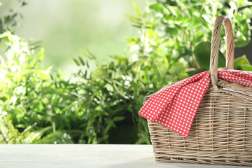 Closed wicker picnic basket on white wooden table against blurred background, space for text