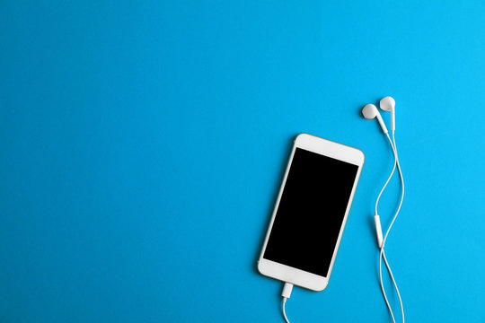 Modern Phone With Earphones On Blue Background, Top View. Space For Text