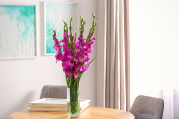 Vase with beautiful pink gladiolus flowers on wooden table in room, space for text