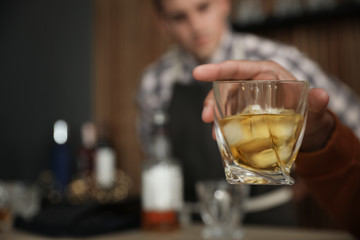 Young man with glass of whiskey in bar, closeup. Space for text