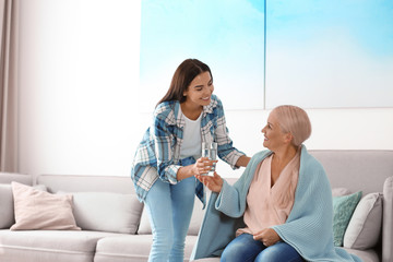 Daughter giving glass of water to her mother at home. Help concept
