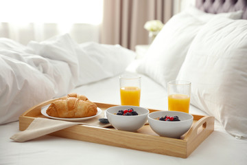 Tray with tasty breakfast on bed in light room - obrazy, fototapety, plakaty