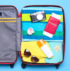 Naklejka premium Open suitcase with beach objects on blue background, top view
