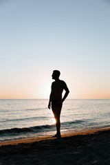 Fototapeta na wymiar Silhouette of a young man enjoying beautiful sunset on the beach 