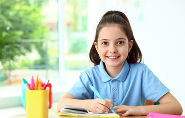 Little girl doing assignment at desk in classroom. School stationery