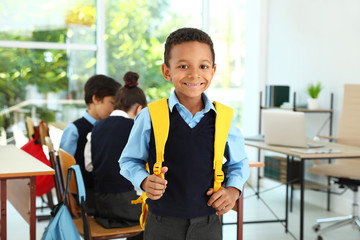 African-American boy wearing school uniform with backpack in classroom - Powered by Adobe
