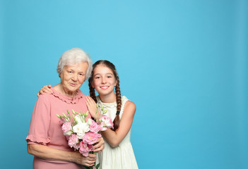 Cute girl and her grandmother with flowers on light blue background. Space for text