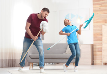 Dad and son having fun while cleaning living room together