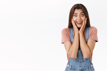 Excited, surprised happy girl cheering as heart fantastic news, touching face astonished, smiling joyfully, stare camera processing unbelievable awesome info, standing white background