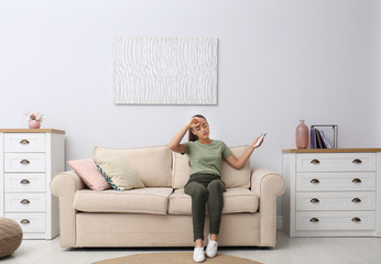 Young woman switching on air conditioner with remote control at home