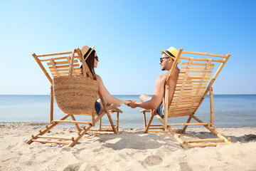 Young couple relaxing in deck chairs on beach