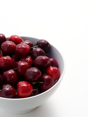 A bowl full of freshly washed cherries on white.