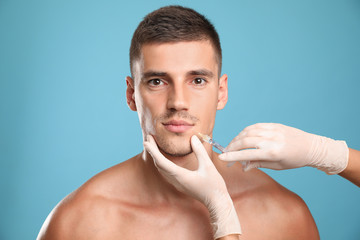 Man getting facial injection on light blue background. Cosmetic surgery