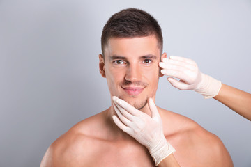 Doctor examining man's face for cosmetic surgery on grey background