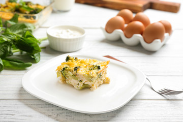 Piece of tasty broccoli casserole on white wooden table