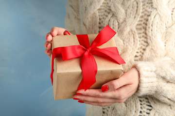 Young woman holding Christmas gift on blue background, closeup