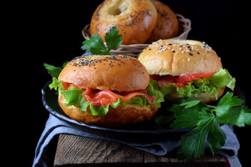 Bagel sandwich with smoked salmon and lettuce salad on black plate