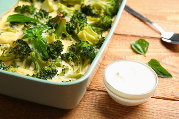 Tasty broccoli casserole served with sour cream on wooden table