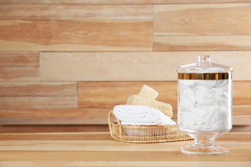 Fototapeta na wymiar Decorative glass jar with cotton pads and bathroom accessories on table against wooden background. Space for text