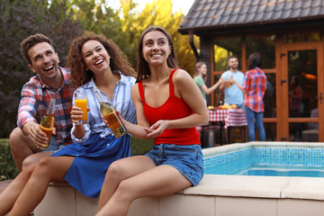Happy friends with drinks at barbecue party near swimming pool outdoors