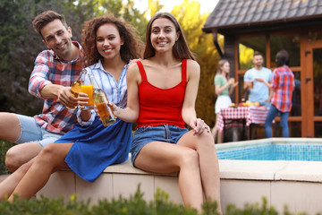 Happy friends with drinks at barbecue party near swimming pool outdoors