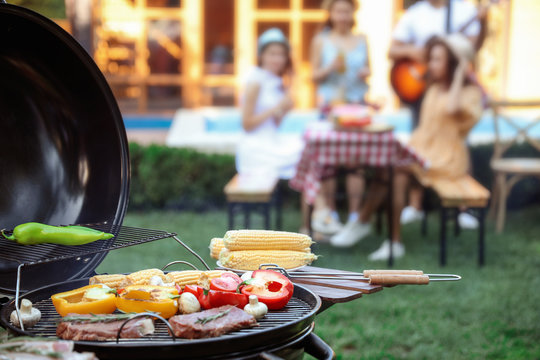 Barbecue grill with tasty fresh food and blurred people on background