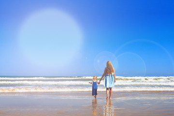 Mom and daughter are walking on the beach. Back view, copy space.