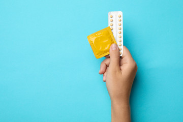 Woman holding condom and birth control pills on blue background, top view with space for text. Safe...