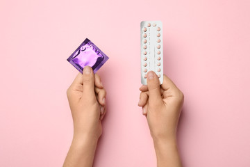 Woman holding condom and birth control pills on pink background, top view. Safe sex