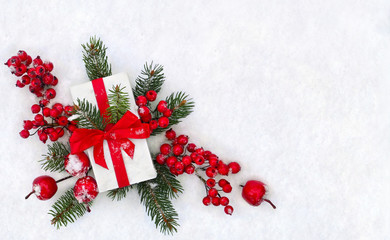 Christmas decoration, banner. Gift box with red ribbon, bow, twigs christmas tree, red berries and apples on snow with space for text. Top view, flat lay