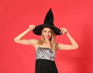 Beautiful young woman wearing witch costume for Halloween party on red background