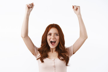 Waist-up shot cheerful enthusiastic redhead girl pump her fist joyfully, celebrating amazing news,...