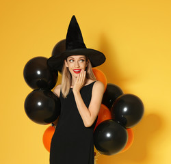 Beautiful woman wearing witch costume with balloons for Halloween party on yellow background, space for text