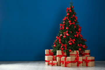 Decorated Christmas tree and gift boxes near blue wall. Space for text