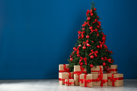 Decorated Christmas tree and gift boxes near blue wall. Space for text
