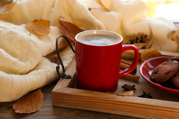 Composition with cup of hot drink, sweater and autumn leaves on windowsill. Cozy atmosphere