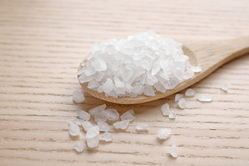 Spoon with white sea salt on wooden table, closeup. Spa treatment