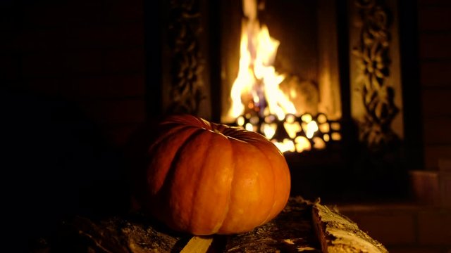 Halloween pumpkin lying in the dark on birch logs. In the background are flames bursting out of the fireplace insert.